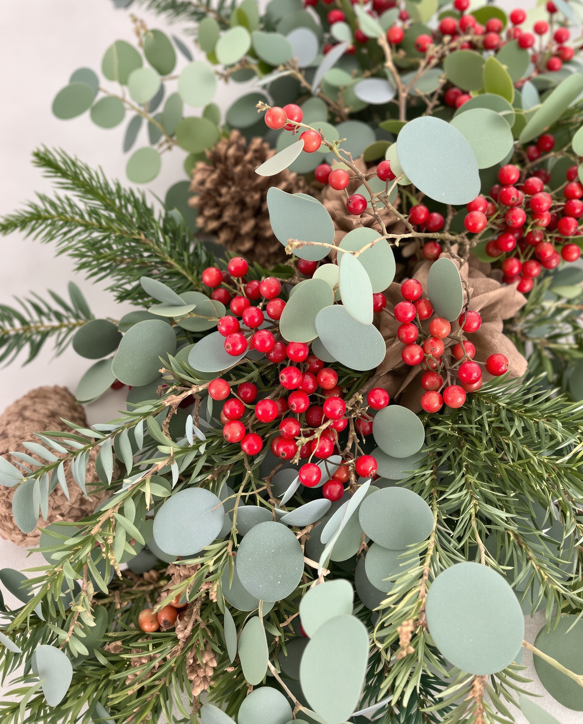 Éléments naturels centre de table Noël : branches de sapin, eucalyptus, pommes de pin, baies rouges. Ambiance récup et festive.