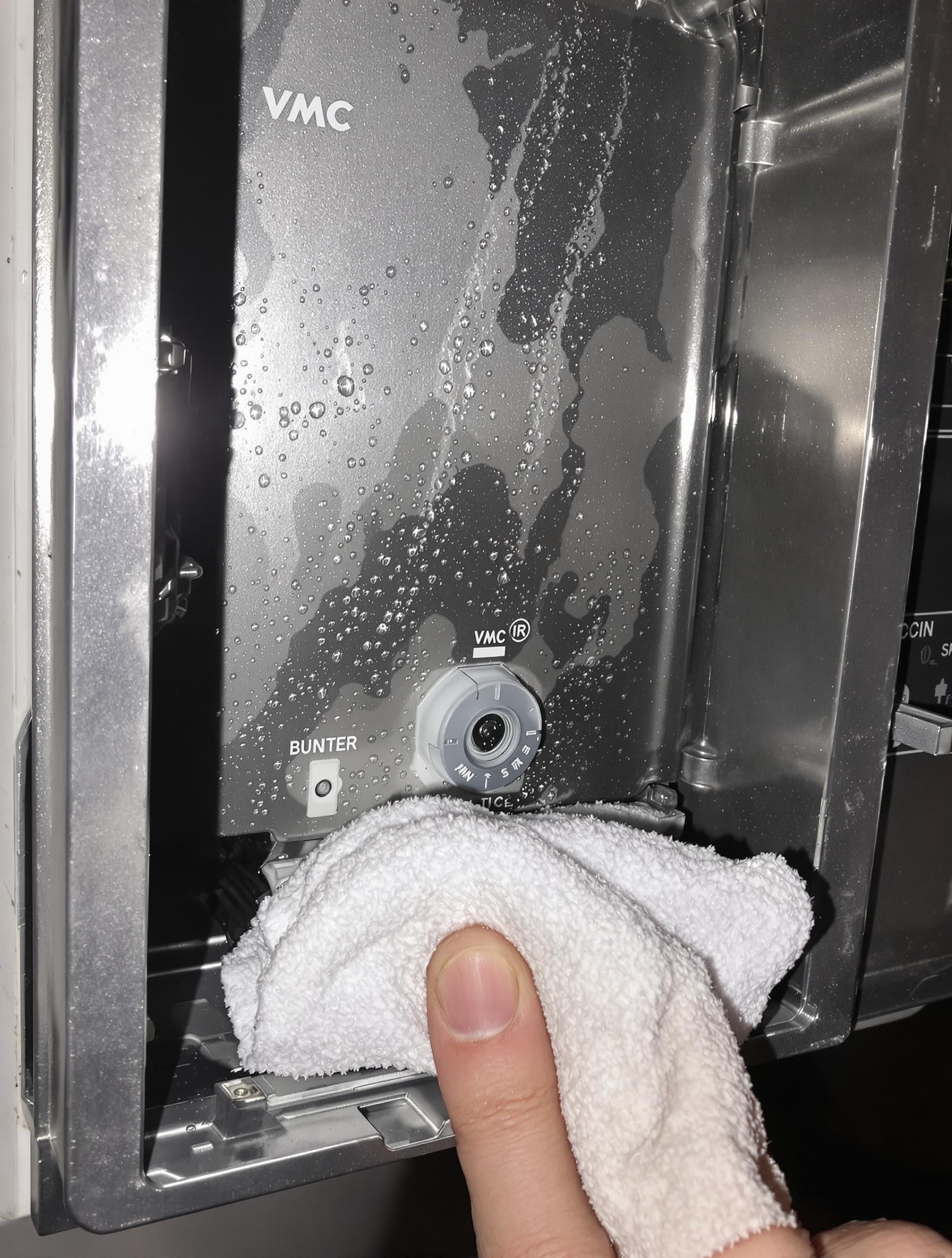 Caisson VMC ouvert avec condensation visible et une main essuyant les poches d'eau.