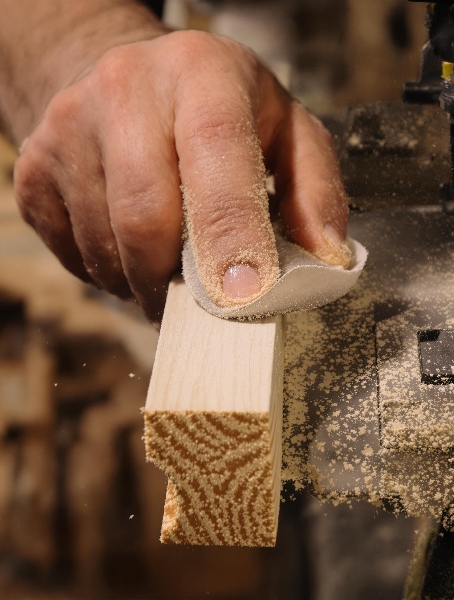 Gros plan sur le ponçage des arêtes d’une plinthe en bois avec du papier émeri.